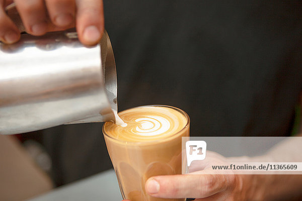 Nahaufnahme der Hände des Barista  der im Café Milch in den Kaffee gießt