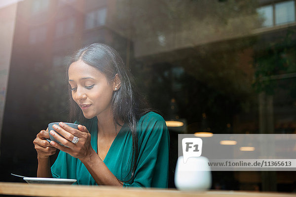 Mittlere erwachsene Frau im Café-Fenstersitz mit Blick auf die Kaffeetasse