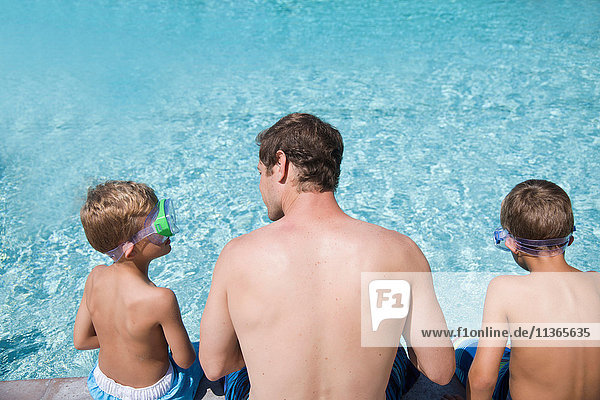 Rear view of man and two sons sitting on poolside in scuba goggles  Laguna Beach  California  USA