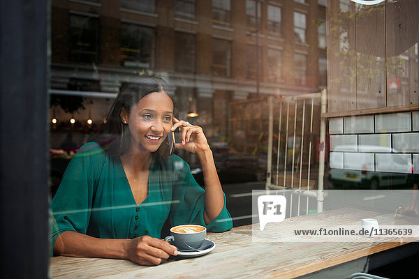 Mittlere erwachsene Frau beim Plaudern auf dem Smartphone im Café-Fenstersitz