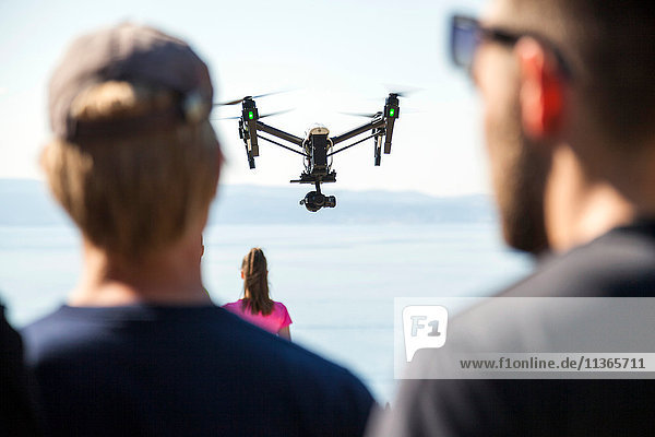 Rückansicht eines Mannes und einer Frau mit Blick auf eine Drohne  die mitten in der Luft über der Küste fliegt  Split  Dalmatien  Kroatien