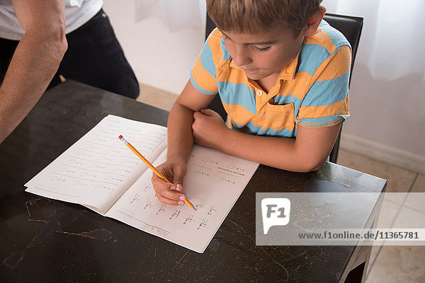 Junge mit Vater beim Schreiben im Hausaufgabenbuch am Tisch