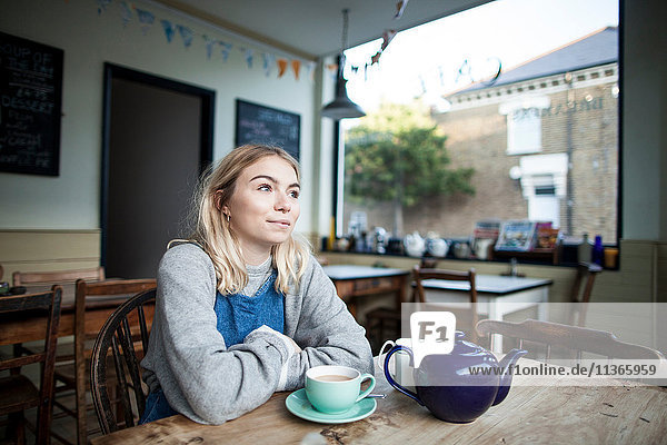 Junge Frau im Café sitzend  Tasse Tee und Teekanne auf dem Tisch  nachdenklicher Ausdruck