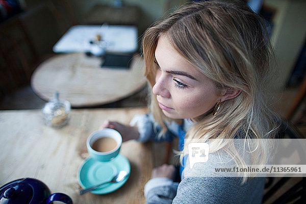 Young woman sitting in cafe  holding tea cup  thoughtful expression on face