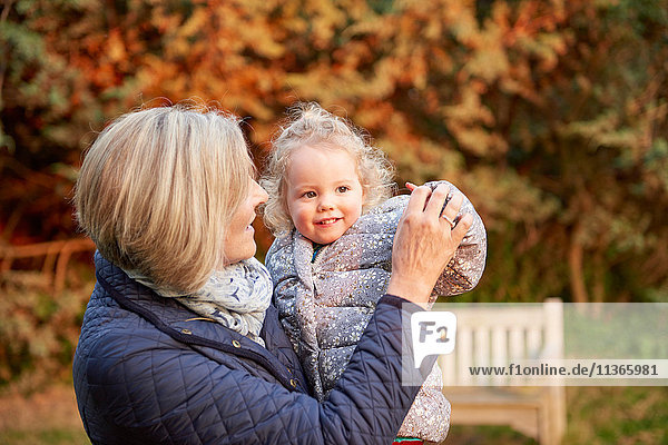 Ältere Frau trägt Kleinkind-Enkelin im Herbstpark
