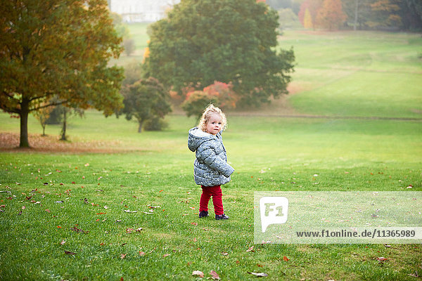 Porträt eines weiblichen Kleinkindes  das im Herbst im Park über die Schulter schaut