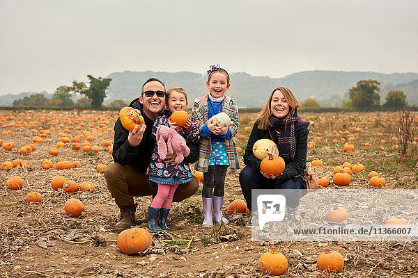 Portrait of parents and two daughters crouching in pumpkin field