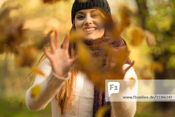 Junge Frau wirft Herbstblätter in die Luft und lächelt