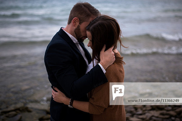Romantisches Paar mittlerer Erwachsener umarmt sich in der Abenddämmerung am Strand