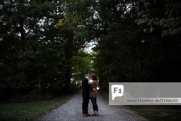 Romantisches Paar mittlerer Erwachsener umarmt sich in der Abenddämmerung auf ländlicher Strecke