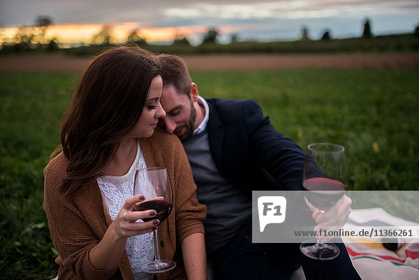 Romantisches Paar mit Rotwein  das sich bei Sonnenuntergang auf einer Picknickdecke im Feld entspannt