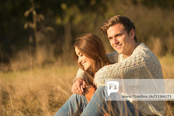 Junges Paar sitzt in ländlicher Umgebung und lächelt