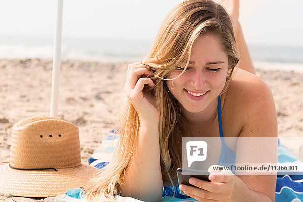 Junge Frau benutzt Mobiltelefon am Strand