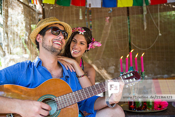 Junges Paar spielt lächelnd Gitarre