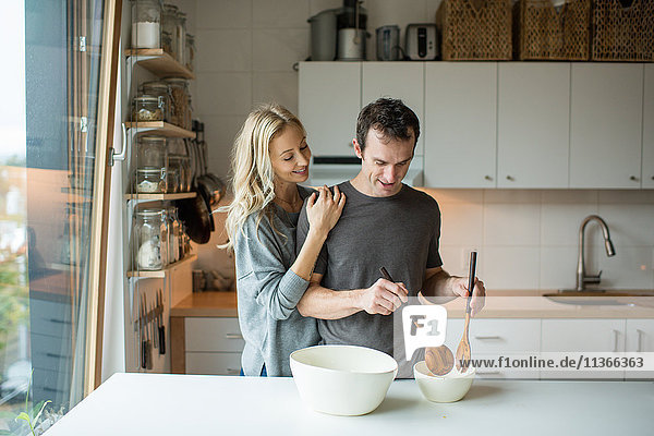 Mittleres erwachsenes Paar beim Mischen von Salatschüsseln in der Küche
