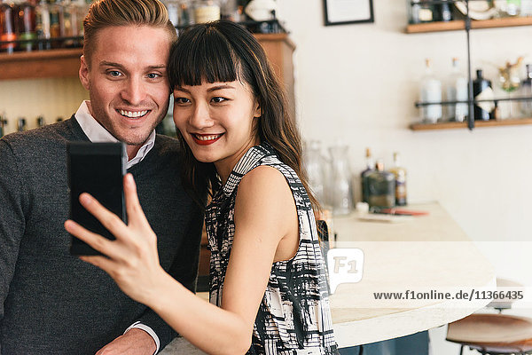Young couple taking smartphone selfie in cocktail bar