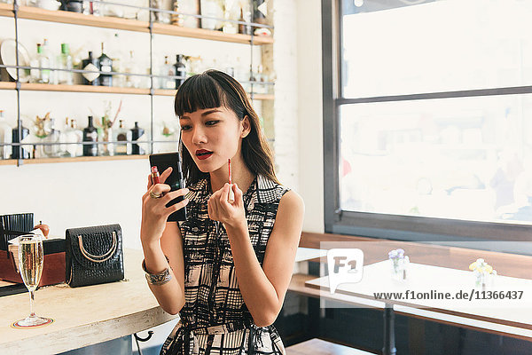 Junge Frau trägt Lippenstift in der Cocktailbar auf