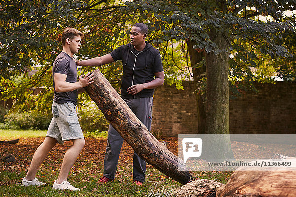 Junger Mann mit Personal Trainer beim Anheben des Baumstammes im Park