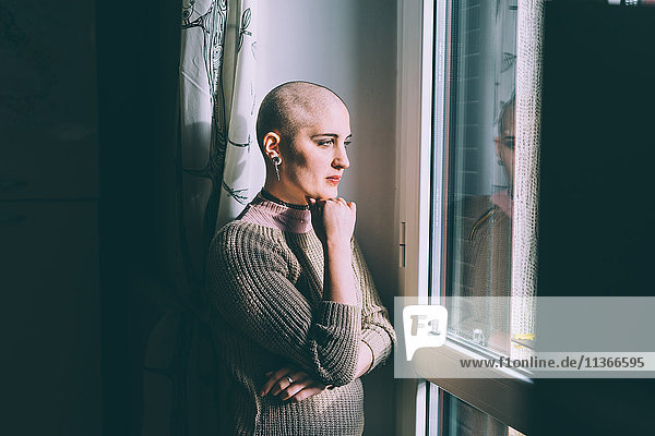 Porträt einer jungen Frau mit rasiertem Kopf  die durchs Fenster blickt.
