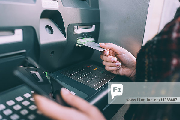 Hand der jungen Frau beim Einstecken der Kreditkarte in den Geldautomaten