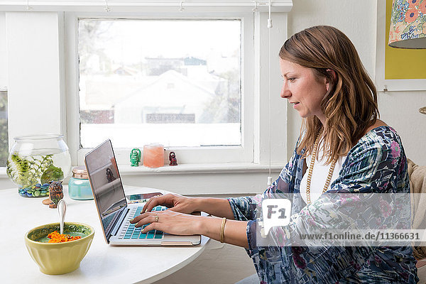 Frau sitzt mit Laptop am Esstisch