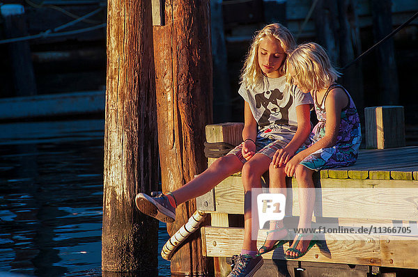 Mädchen sitzen Seite an Seite auf dem Pier