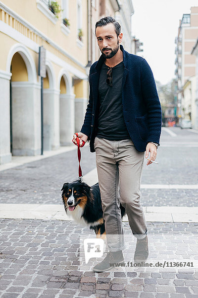 Mittelgroßer Mann geht mit seinem Hund in gepflasterter Stadtstraße spazieren