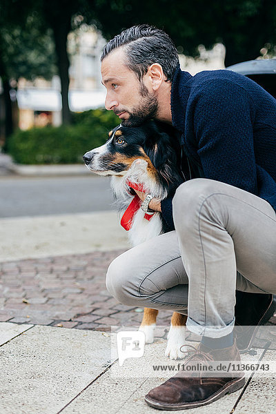 Mittelgroßer erwachsener Mann kauert mit Haushund auf dem Bürgersteig der Stadt