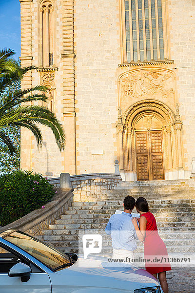 Rückansicht eines jungen Paares mit Cabriolet beim Blick auf die Karte  Calvia  Mallorca  Spanien