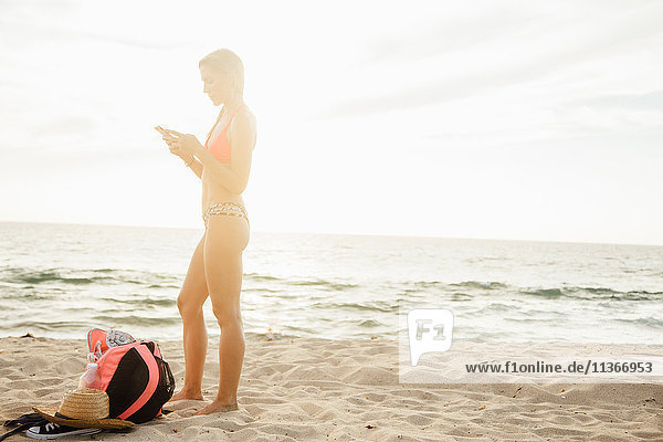 Frau am Strand schaut auf Smartphone