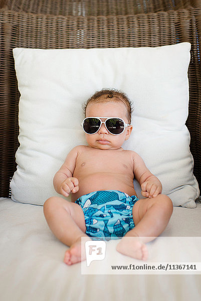 Baby mit Sonnenbrille auf Rattan-Stuhl sitzend