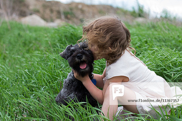 Kleines Mädchen küsst Haushund auf Grasfeld