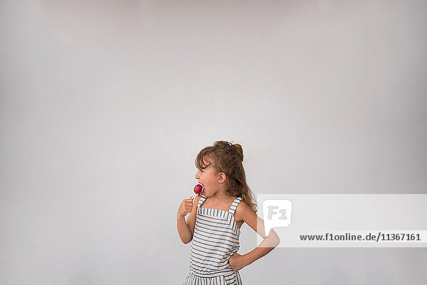 Kleines Mädchen leckt Lolli vor weißem Hintergrund