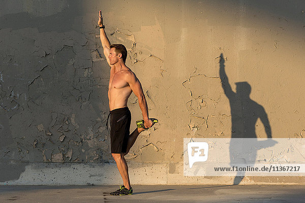 Männlicher Athlet streckt sich vor Betonwand