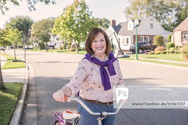 Portrait of youthful senior woman with bicycle on suburban road