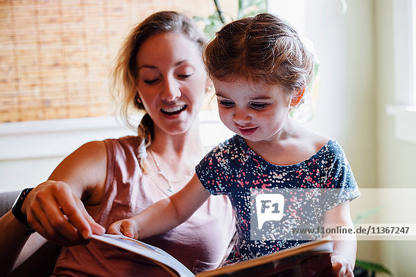 Frau auf Sofa mit Kleinkind Tochter liest Märchenbuch