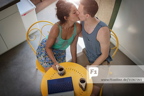 High angle view of romantic young couple kissing at kitchen table