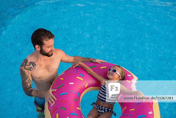 Junges Mädchen im Schwimmbad  entspannt auf aufblasbarem Ring  Vater steht neben ihr