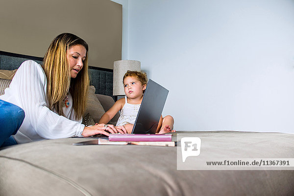 Mother using laptop on bed with daughter