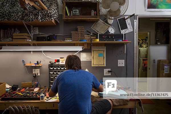 Rear view of guitar maker sitting at desk manufacturing guitar