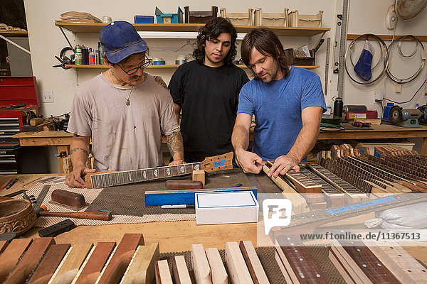Guitar makers in workshop quality checking guitar necks