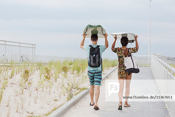 Rear view of young couple carrying surfboards on heads  Rockaway Beach  New York State  USA