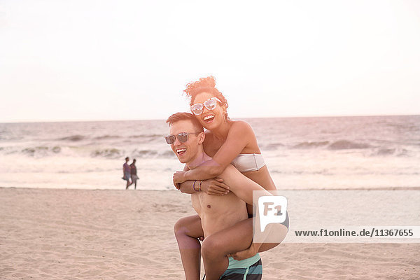 Young man giving piggy back to girlfriend on Rockaway Beach  New York State  USA