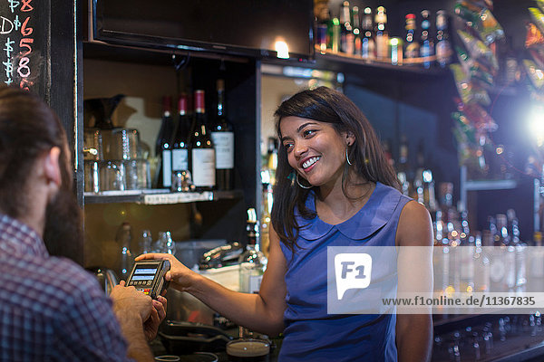 Male customer paying by credit card machine to barmaid in public house