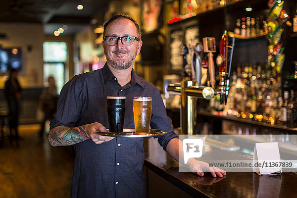 Portrait of mature bartender carrying tray of beer in public house