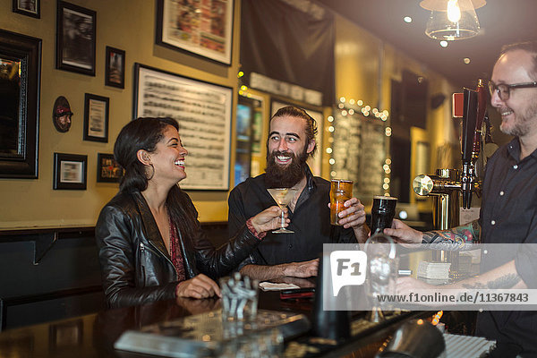 Bartender and young couple raising a toast in public house