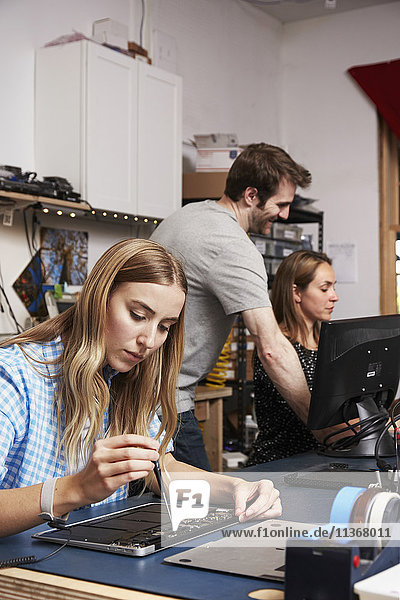 A man standing behind two women sitting working on circuitry in a technology lab.