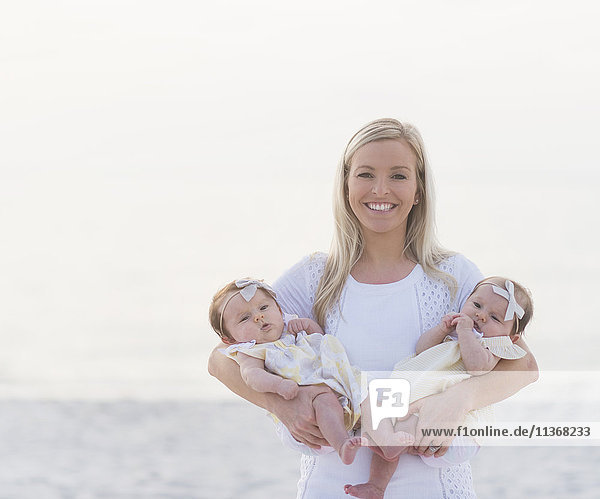 Porträt einer glücklichen erwachsenen Mutter mit zwei kleinen Mädchen (2-5 Monate)