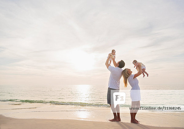 Happy family with two baby girls (2-5 months) at beach in sunlight