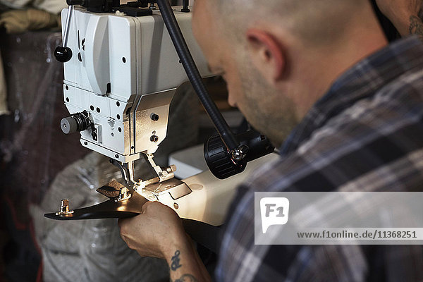 Ein Mann  der eine Industrienähmaschine benutzt und handgefertigte Lederwaren näht.